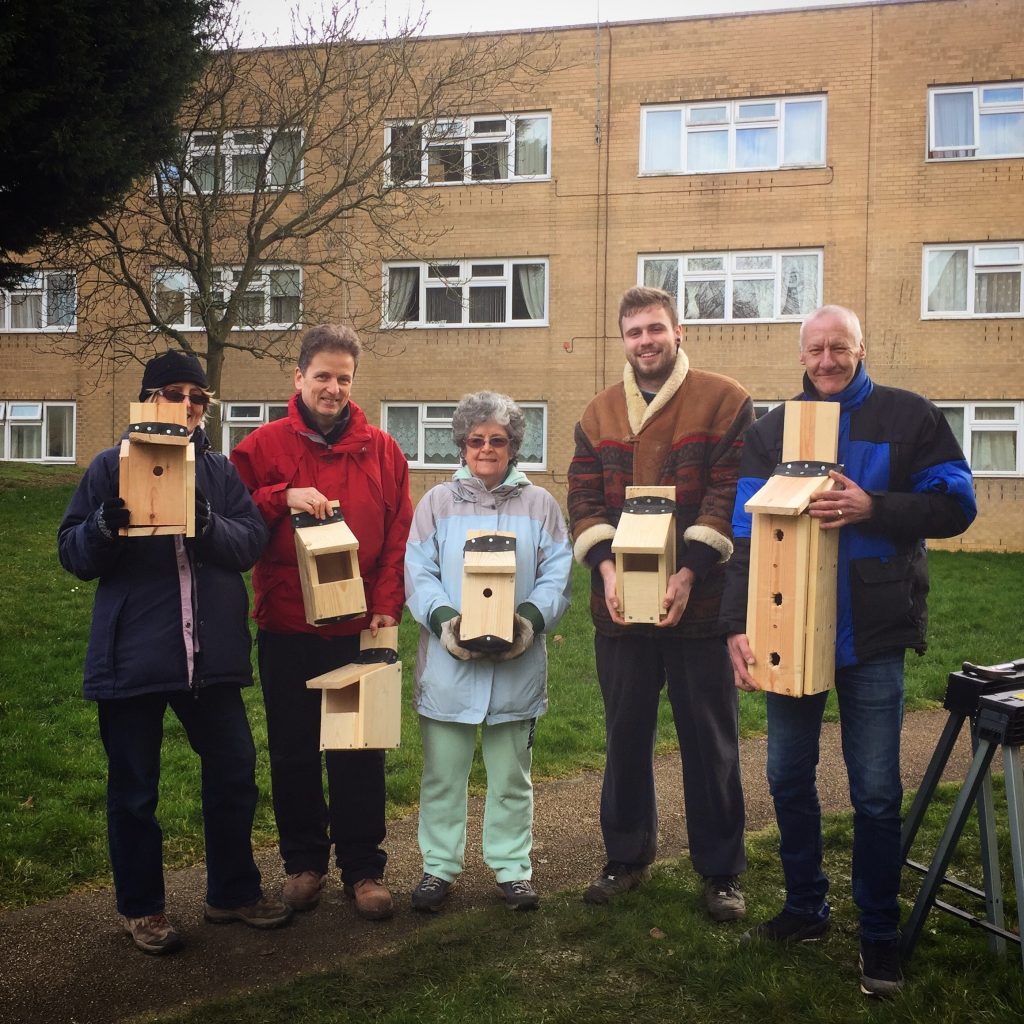 Group of people holding homemade bird boxes in front a flats