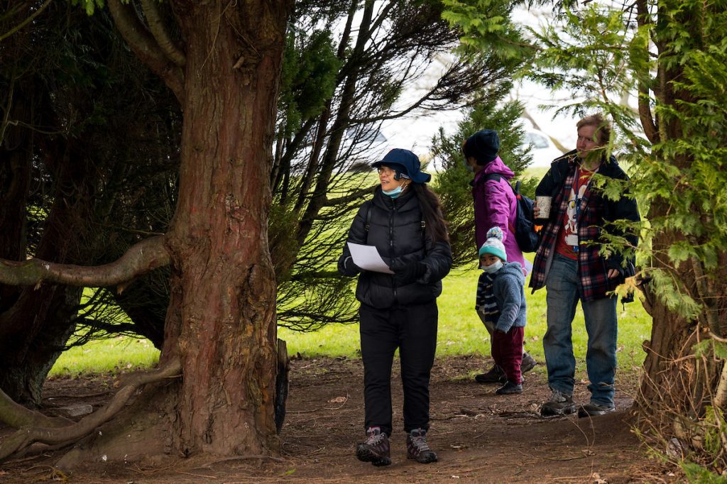 A group of mask-wearing people including a child walking through woodland