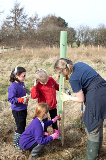 Children from Wheldrake with Thorganby CE Primary School planting a tree in a grassy area.