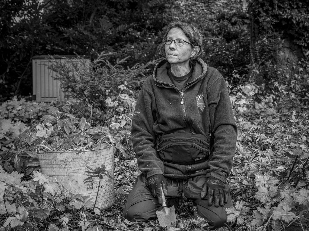 Black and white image of a lady with trowel surrounded by leaves and vegetation. Credit Mark Slater, TCV