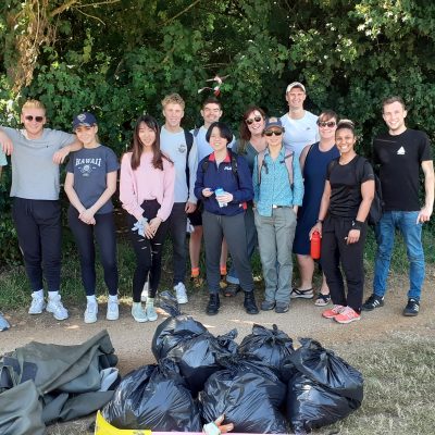 Group of people stood under a tree on a path. They are looking at the camera and smiling. On the bath in front of them is a pile of black bin bags