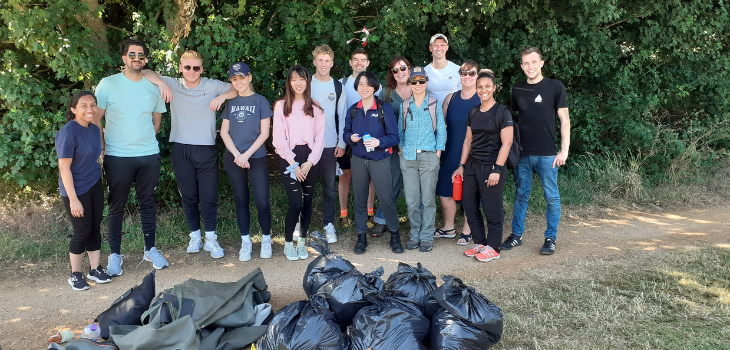 Group of people stood on a path in front of a hedgerow. They are all looking at the camera and smiling. On the path in front of them is a pile of black bin bags