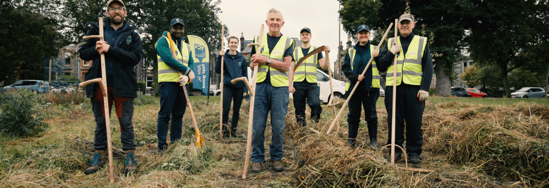 Group of TCV volunteers in woodland wearing high viz jackets and holding gardening tools