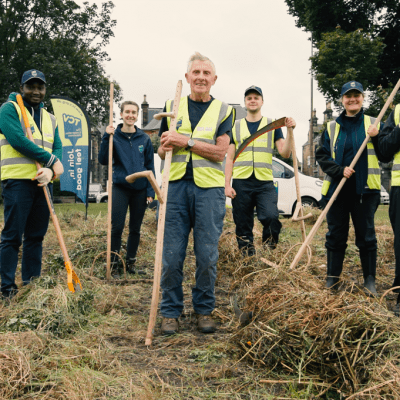 Group of TCV volunteers in woodland wearing high viz jackets and holding gardening tools