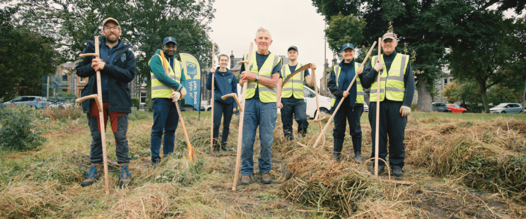 Group of people in high viz vests holding tools to clear a green space