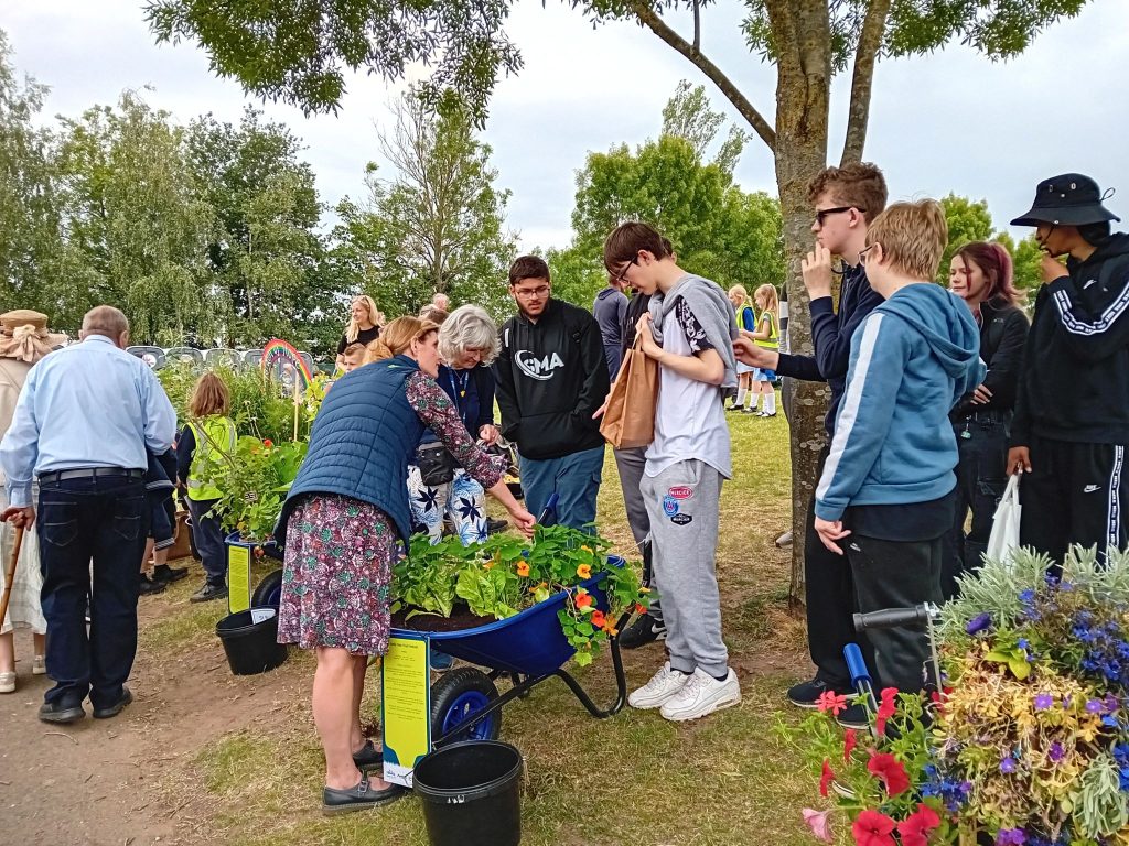 Group of people admiring flowers in a wheelbarrow.