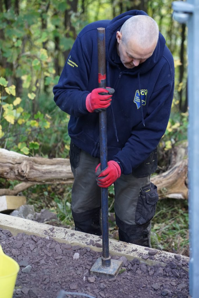 Man wearing a blue TCV top using a tool to flatten soil