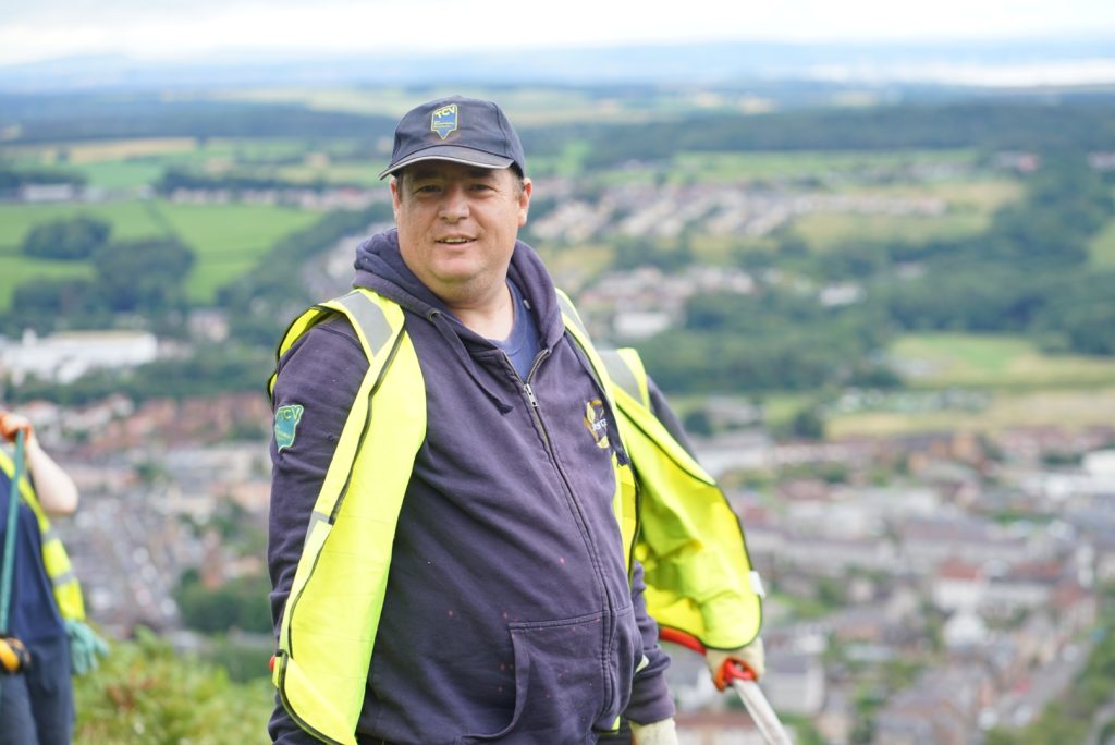 Man wearing a high vis top and cap against a background of lots of houses and fields.