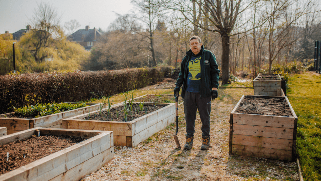 A man stands in front of well-maintained raised garden beds, ready for planting vegetables.
