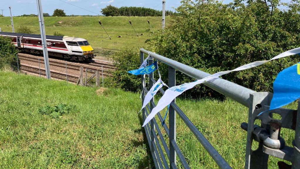 A metal gate with TCV bunting and moving train in the background